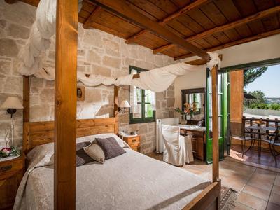 Rustikales Schlafzimmer mit Holzbalken, Steinwand und Blick auf die Terrasse und das Meer.