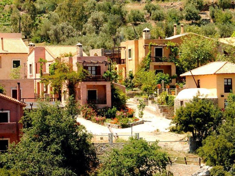 Kleine Dorfgruppe mit farbigen Häusern, umgeben von dichtem, grünem Wald auf hügeligem Gelände.