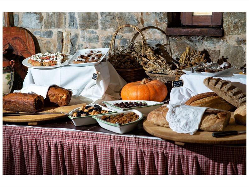 Ein gedeckter Tisch mit verschiedenen Broten, Gebäcken und einem Kürbis vor Steinwand.