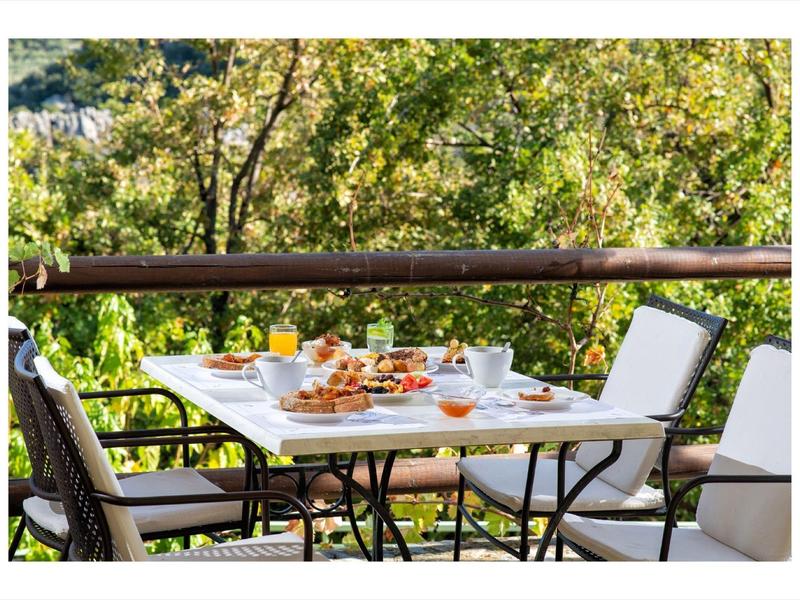 Ein gedeckter weißer Gartentisch mit Stühlen auf Balkon, umgeben von grünem Laub.