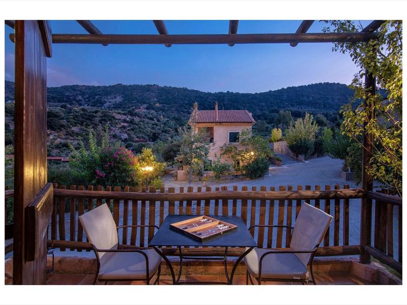 Balkon mit zwei Stühlen und Tisch, sichtbarer Garten und Haus vor bewaldeten Hügeln bei Abenddämmerung.