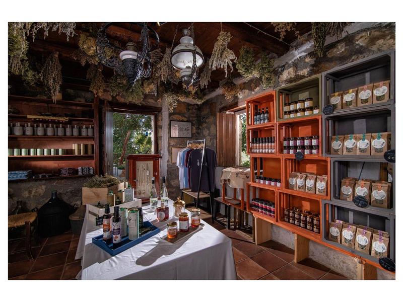 Rustikaler Laden mit Holzmöbeln, Gewürzregalen, Glaslampen und einem weißen Tisch mit Produkten.