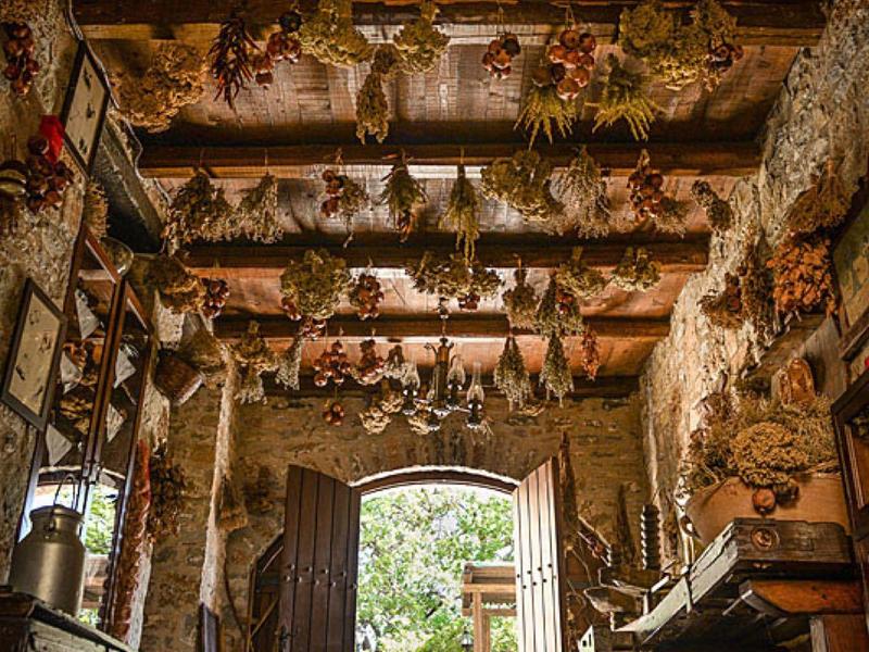 Rustikaler Raum mit getrockneten Kräutern an Decke und Wänden, Licht am offenen Holztor.