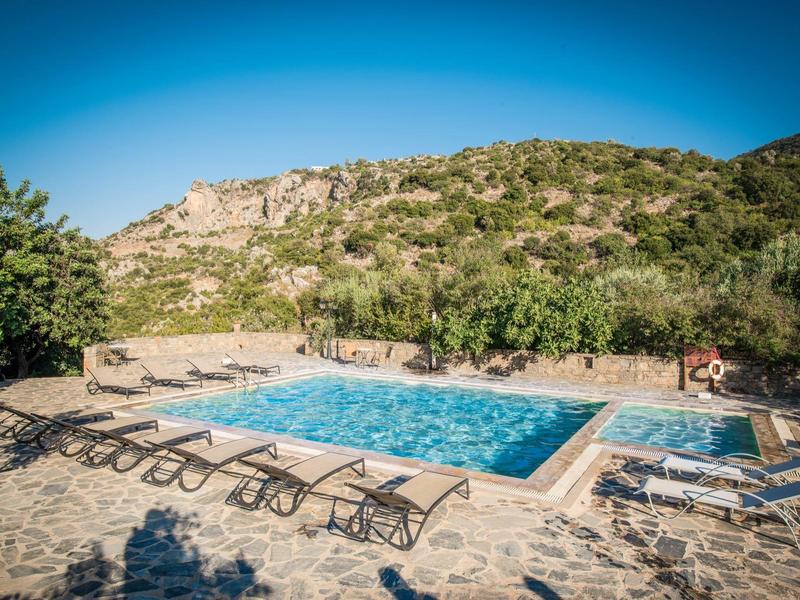 Pool mit Liegestühlen und umliegender Natur vor einem Berg unter klarem Himmel