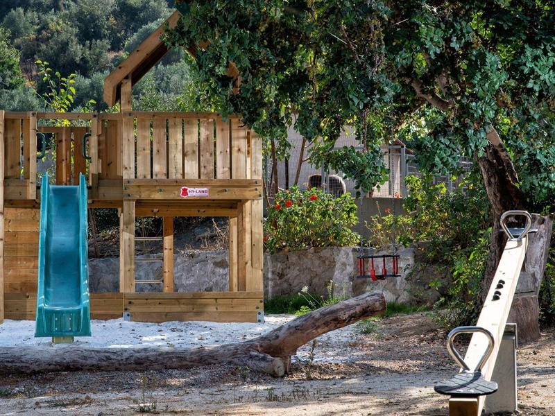 Kinderspielplatz mit Holzhütte, Rutsche und Schaukel in einer bewaldeten Umgebung.