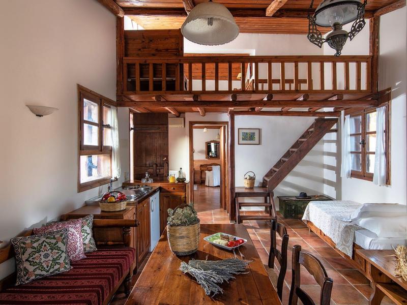 Gemütlicher Wohnbereich mit Holzmöbeln, Treppe zu einer Galerie und großen Fenstern.