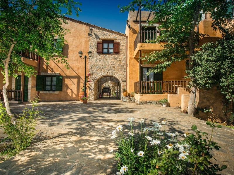 Innenhof eines charmanten, sonnigen Hotels mit mediterranem Baustil und Blumen im Vordergrund.