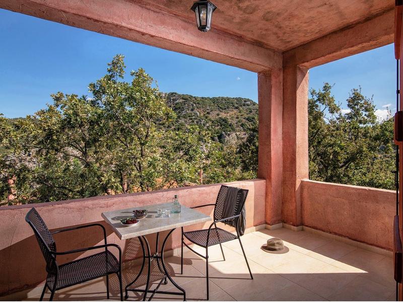 Überdachte Terrasse mit Tisch, zwei Stühlen und Blick auf bewaldeten Hügel.