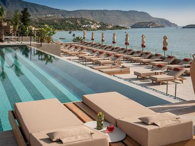 Poolbereich mit Liegestühlen und Sonnenschirmen mit Blick auf das Meer und die Berge.
