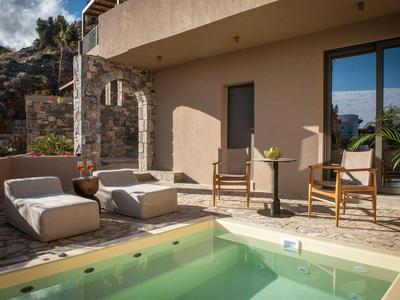 Moderní venkovní prostor s bazénem, židlemi, pohovkou a horským pozadím u hotelového pokoje.