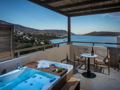 Balcón con jacuzzi, mesa y sillas con vistas al mar y las colinas en el horizonte.