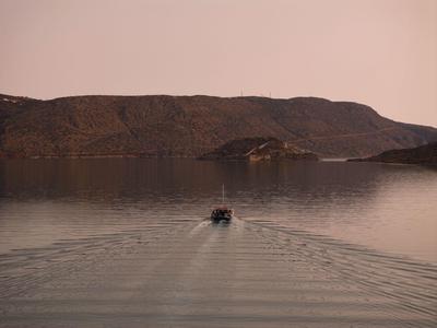 Boot fährt bei Sonnenuntergang über ruhiges Wasser mit Hügeln im Hintergrund.
