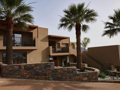 Moderne Gebäude mit Balkonen und Palmen in einem Hotelresort bei Sonnenuntergang.