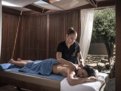 Frau erhält Massage auf einem Massagetisch in einem offenen, holzverkleideten Raum mit Tageslicht.