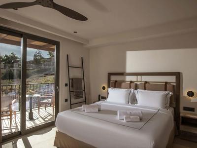 Habitación de hotel luminosa con cama grande, puerta a la terraza y balcón con vistas al paisaje natural.