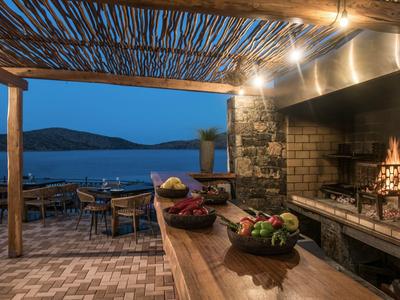 Gemütlicher Außenbereich mit rustikalem Grillplatz und Ausblick auf das Meer bei Dämmerung.