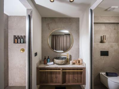 Modernes Badezimmer mit Waschbecken, rundem Spiegel und Duschbereich mit Glaswand.