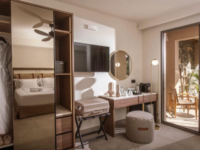 Modern eingerichtetes Hotelzimmer mit Schreibtisch, Fernseher und Balkon mit Pflanzen.