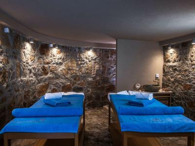 Ein entspannter Wellnessraum mit zwei Massageliegen und blauem Tuch vor einer rustikalen Steinwand.