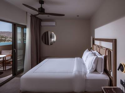 Modernes Hotelzimmer mit großem Bett und Balkon mit Sitzbereich und Meerblick.