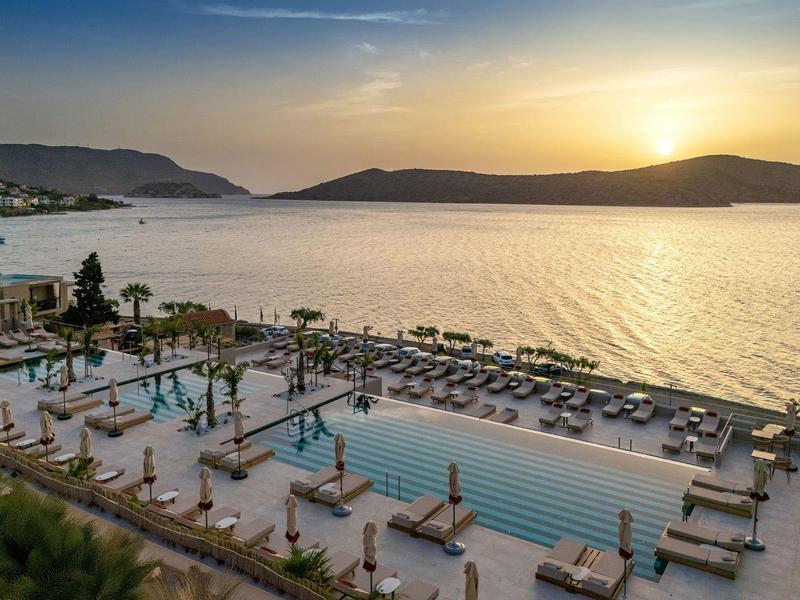 Lujosa piscina exterior junto al mar con tumbonas y vista al atardecer.