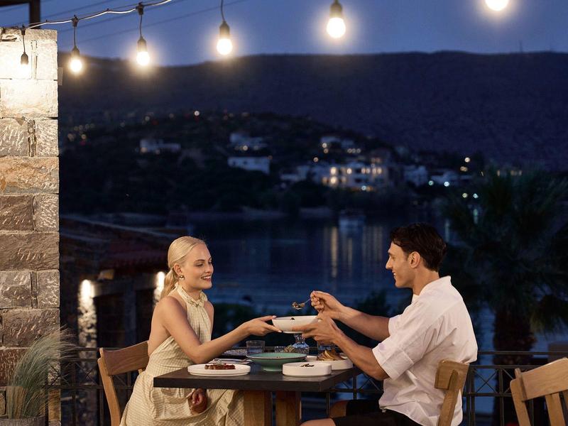 Pareja sentada en mesa exterior puesta por la noche con luces decorativas.