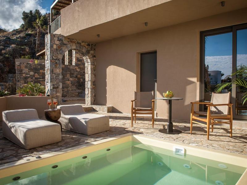 Moderní venkovní prostor s bazénem, židlemi, pohovkou a horským pozadím u hotelového pokoje.