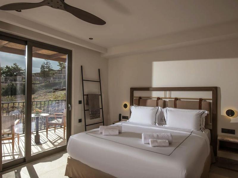 Habitación de hotel luminosa con cama grande, puerta a la terraza y balcón con vistas al paisaje natural.