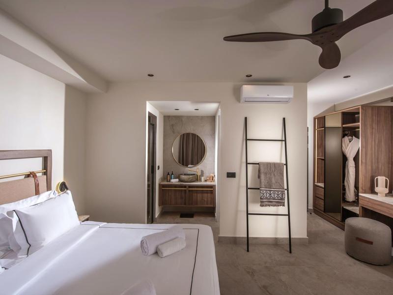 Moderní hotelový pokoj s velkou postelí, stropním ventilátorem a otevřeným koupelnovým prostorem.