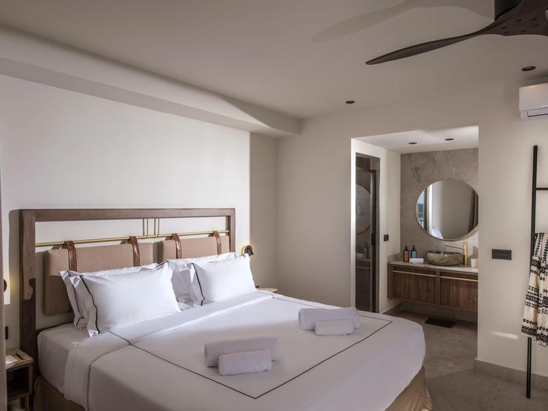 Moderní hotelový pokoj s velkou manželskou postelí, stropním ventilátorem a otevřenou koupelnou.