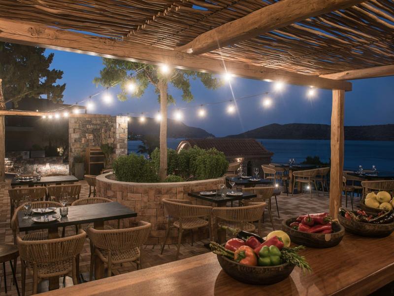 Pohodlná terasa se stolky, dekorativními světly a výhledem na moře za soumraku.