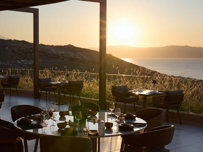 Abendliche Terrassenansicht eines Restaurants mit Blick auf Hügel und Meer im Sonnenuntergang.
