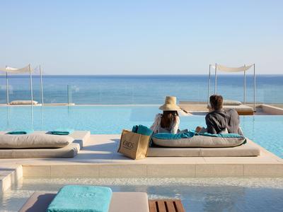 Two people relaxing on loungers by an infinity pool overlooking the sea.