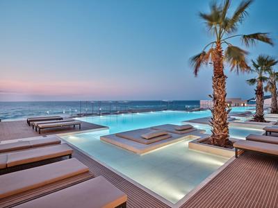 Infinity pool with loungers and palm trees at sunset by the sea at a hotel.