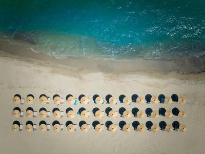 Luchtfoto van ligstoelen op het strand naast turquoise water.