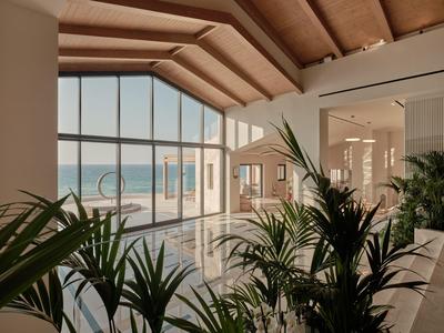 Bright hotel lobby with large glass windows, plants, and a sea view.