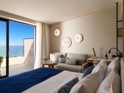 Bright hotel room with sea view, double bed, gray sofa, and modern wall decor.