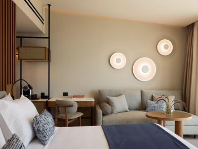 Modern hotel room with bed, sofa, desk, and decorative wall lights.