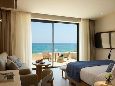 Modern hotel room with sea view, beige sofa, and double bed with blue throw.