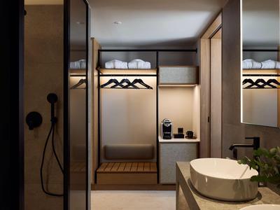 Modern hotel room entrance with open wardrobe and bathroom area in warm lighting.