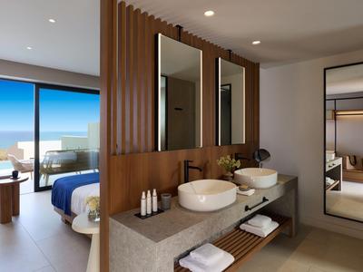 Modern hotel room with open bathroom, two sinks, and a terrace view overlooking the sea.