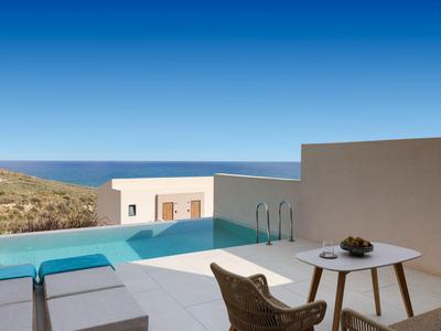 Modern hotel pool with sea view and terrace with chairs and table under clear sky.