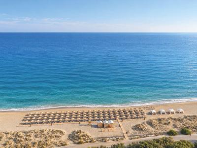 A wide sandy beach with rows of sun umbrellas and a view of the calm blue sea.