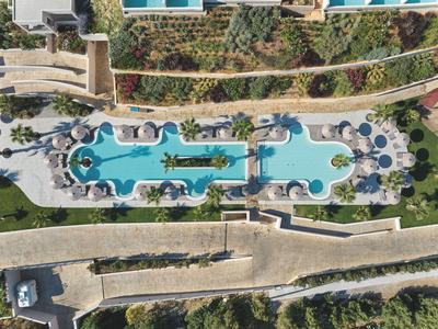 Aerial view of two connected hotel pools with sun loungers, palm trees, and adjacent walkway.