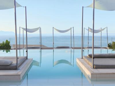 Luxurious pool area with cozy beds and sea view under clear sky.