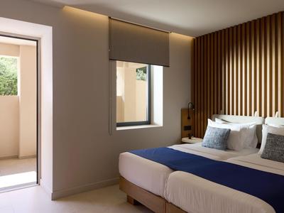 Modern hotel room with two beds, wooden panels, and access to a balcony.