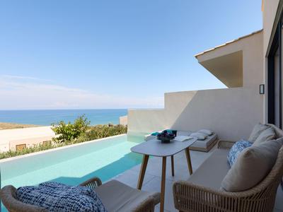 Terrace with pool, chairs, and a sea view on a sunny day.