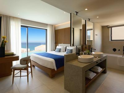 Bright hotel room with large bed, sea view, and modern bathroom featuring double sinks.