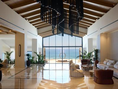 Elegant hotel lobby with high ceilings, large windows, and sea view.