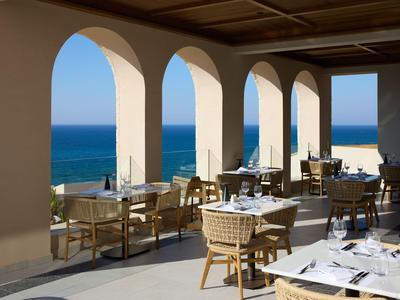 Open dining area with wicker chairs overlooks blue ocean and sky through large arches.